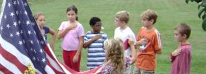 students pledge allegiance with stars and stripes flag on left