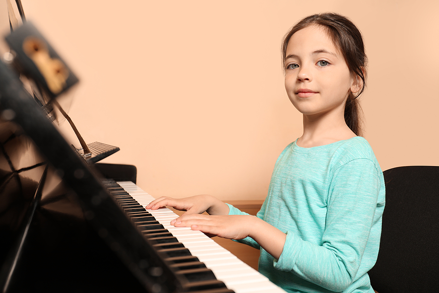 Cute Little Girl Playing Piano Near Beige Wall. Music Lesson girl playing piano