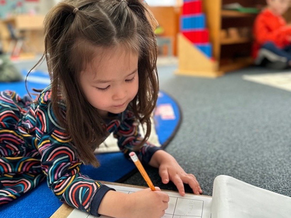 girl in a Montessori class on the floor practicing writing