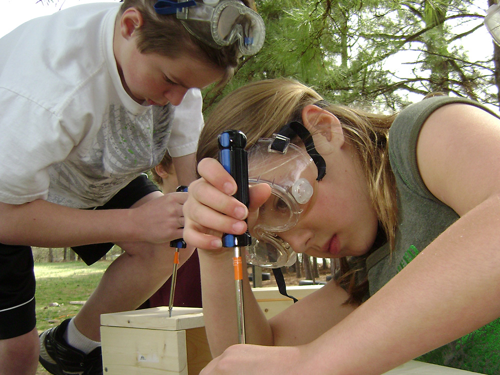 two Montessori middle school students doing woodwork outdoors